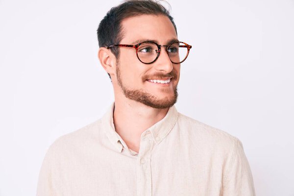 Young handsome man wearing casual clothes and glasses looking away to side with smile on face, natural expression. laughing confident. 