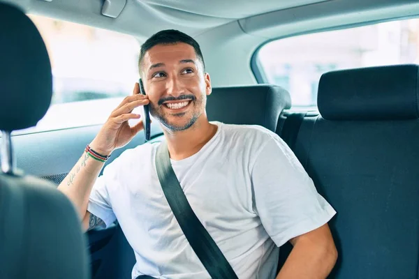 若いヒスパニック系の男は車の上に座っているスマートフォンで幸せな話を笑って — ストック写真