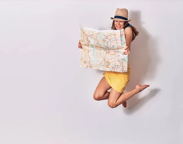Young beautiful girl wearing bikini and summer hat smiling happy. Jumping with smile on face holding city map over isolated white background