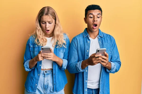 スマートフォンを使用して若い異人種間のカップルは恐れて 驚きと驚きの表情でショックを受けました 恐怖と興奮した顔 — ストック写真