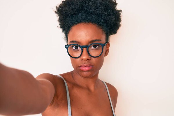 Young african american woman wearing casual clothes and glasses making selfie by the camera thinking attitude and sober expression looking self confident 