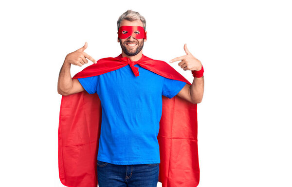 Young blond man wearing super hero custome looking confident with smile on face, pointing oneself with fingers proud and happy. 