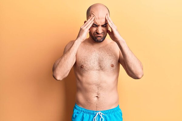 Young handsome bald man wearing swimwear shirtless with hand on head, headache because stress. suffering migraine.