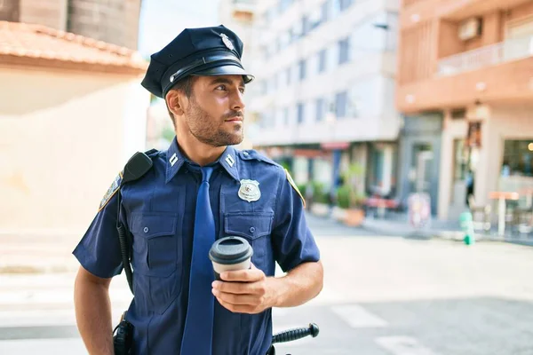 Genç İspanyol polisi ciddi bir ifadeyle polis üniforması giyiyor. Kasaba caddesinde dikilmiş kahve içerken.