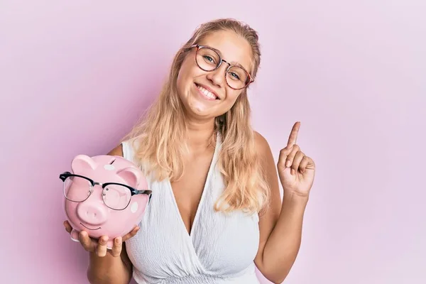 Jong Blond Meisje Holding Piggy Bank Met Bril Verrast Met — Stockfoto