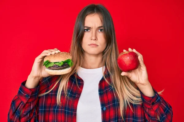 Piękna Biała Kobieta Porównująca Hamburgera Zdrowe Czerwone Jabłko Zrelaksowane Poważnym — Zdjęcie stockowe