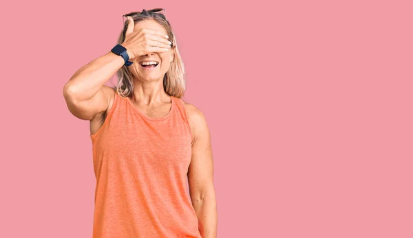 Middle age fit blonde woman wearing casual summer clothes and sunglasses smiling and laughing with hand on face covering eyes for surprise. blind concept.