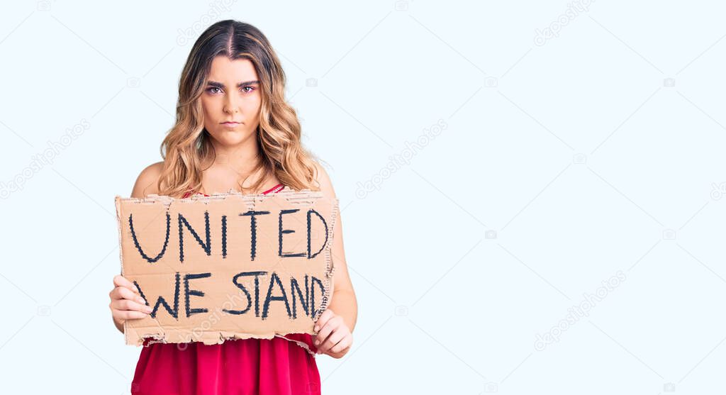 Young caucasian woman holding united we stand banner thinking attitude and sober expression looking self confident 