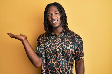 Saçlı, leopar desenli hayvan desenli tişörtlü, neşeli gülümseyen ve avuç içi kameraya bakan Afro-Amerikan bir adam.. 