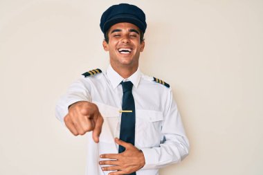 Uçak pilotu üniforması giyen genç İspanyol adam sana gülüyor, eli vücudunun üzerinde kamerayı işaret ediyor, utanç ifadesi. 