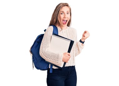 Sırt çantası taşıyan sarışın güzel bir kadın. Elinde not defteri var. Gururla bağırıyor, zaferi kutluyor ve kollarını kaldırarak başarıyı kutluyor. 