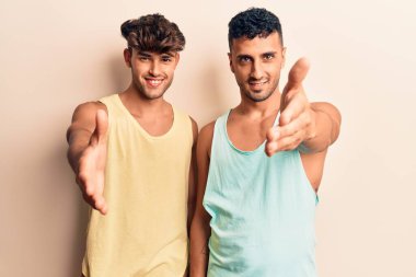 Gündelik giysiler giymiş genç eşcinsel bir çift dostça gülümseyerek selamlama ve hoş geldin demek için tokalaşıyor. başarılı iş. 