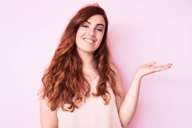 Genç ve güzel bir kadın günlük kıyafetler giyip neşeli bir şekilde gülümsüyor. Elleri avucunun içinde kameraya bakıyor.. 