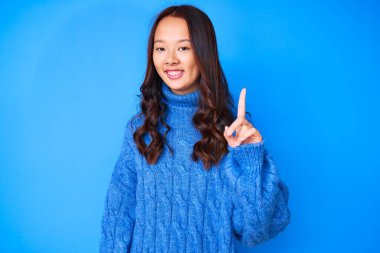 Genç, güzel, Çinli bir kız, sıradan bir kazak giyiyor ve bir numaralı parmağını gösterip gülümsüyor, kendinden emin ve mutlu.. 