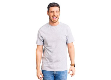 Gündelik tişört giyen yakışıklı genç adam kameraya seksi bir ifadeyle bakıyor, neşeli ve mutlu bir yüzle.. 