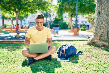 Üniversite kampüsünde çimlerin üzerinde otururken mutlu bir şekilde gülümseyen İspanyol öğrenci.