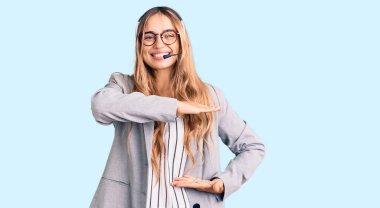 Çağrı merkezi kulaklığı takan genç, sarışın bir kadın. Ellerinde kocaman bir işaret, ölçü sembolü olan el işaretleri var. Kameraya bakıp gülümsüyor. ölçüm kavramı. 