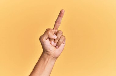 Arm and hand of caucasian man over yellow isolated background showing provocative and rude gesture doing fuck you symbol with middle finger 