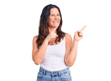 Kolsuz tişört giyen, gülümseyen ve kameraya bakan genç, güzel esmer kadın iki eliyle ve parmaklarıyla kenarı işaret ediyor.. 