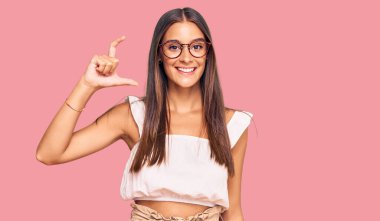 Gündelik kıyafetler giyen, gözlüklü, gülümseyen, kendine güvenen, el hareketi yapan, parmaklarıyla işaret yapan ve kameraya bakan genç İspanyol kadın. ölçüm kavramı. 