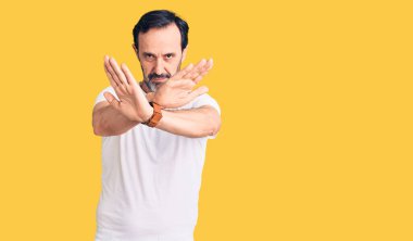 Orta yaşlı yakışıklı bir adam günlük tişört giyiyor. Reddedilmiş yüz ifadesi. Kollarını kavuşturup, avuçlarını çaprazlayarak negatif işaret veriyor. 