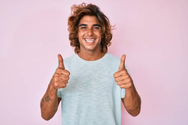 Gündelik kıyafetler giyen genç İspanyol adam. Başarı işareti yapıyor. Elleriyle olumlu jest yapıyor. Neşeli ifade ve kazanan jest. 
