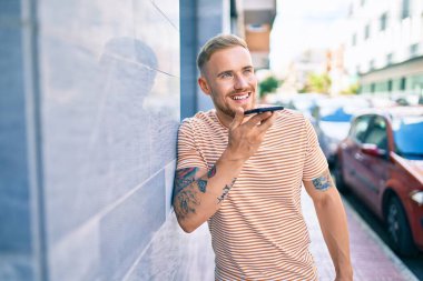 Genç İrlandalı gülümseyen mutlu bir adam şehrin caddesinde akıllı telefonda konuşuyor..