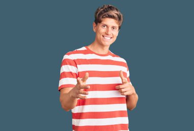 Gündelik giysiler giymiş genç yakışıklı adam mutlu ve komik yüzüyle kamerayı işaret ediyor. iyi enerji ve titreşimler. 