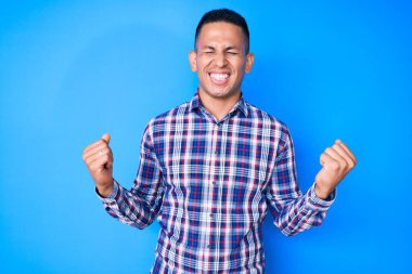 Başarılı olmak için heyecanlı, kolları havada ve gözleri kapalı, gündelik giysiler giyen genç Latin adam zaferi kutluyor. Kazanan konsept. 