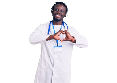 Saç örgülü, doktor steteskobu takan ve kalp sembolü ve elleriyle gülümseyerek kalp sembolü gösteren genç Afro-Amerikan bir adam. romantik kavram. 