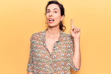 Genç ve güzel İspanyol bir kadın gündelik kıyafetler giyip gülümsüyor bir fikir veya soru işareti ile mutlu bir yüzle, bir numara 