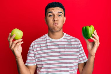 Genç Arap adam elinde yeşil elma ve biberli yanaklarla komik bir yüz tutuyor. Ağzı havayla şişer, havayı yakalar.. 