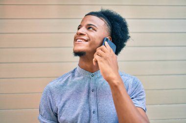 Genç Afrikalı Amerikalı gülümseyen mutlu bir adam şehirdeki akıllı telefondan konuşuyor..