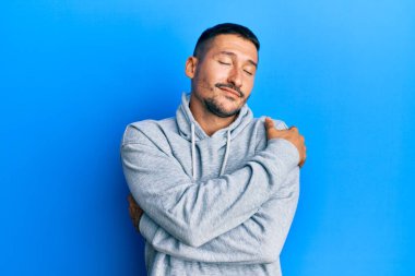 Dövmeleri olan yakışıklı bir adam, sıradan bir kazak giyiyor, kendine sarılıyor, mutlu ve pozitif, kendinden emin gülümsüyor. Sevgi ve özgüven. 