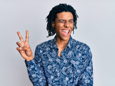 80 'lerin tarzında tişört giyen Afro-Amerikan genç adam kameraya bakıp gülümsüyor ve zafer işareti yapıyor. İki numara.. 