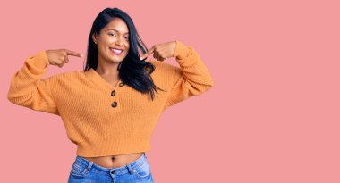 Uzun saçlı, sıradan bir kazak giyen neşeli gülümseyen ve parmaklarıyla ve ağzıyla işaret eden İspanyol bir kadın. diş sağlığı kavramı. 