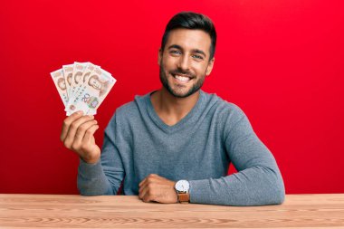 Yakışıklı İspanyol adam Yuan Çin banknotlarını tutuyor. Pozitif ve mutlu görünüyor. Kendine güvenen bir gülümsemeyle dişlerini gösteriyor. 