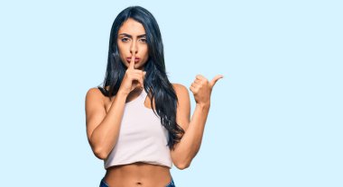 Gündelik kıyafetler giyen güzel İspanyol kadın sessiz olmak istiyor. Parmakları dudaklarında, elleri yana doğru işaret ediyor. sessizlik ve gizli konsept. 