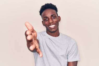 Genç Afro-Amerikan adam günlük kıyafetler giyip gülümseyerek dostça el sıkışarak selamlama ve hoş geldin diyor. başarılı iş. 
