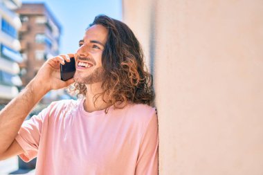 Genç İspanyol adam gülümsüyor. Akıllı telefonda konuşuyor. Duvara yaslanıyor.