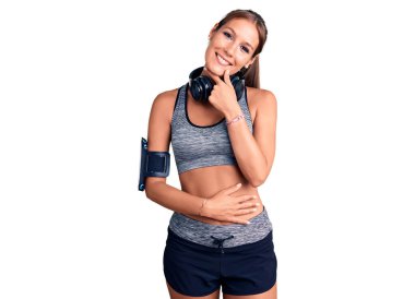 Spor kıyafetleri giyen, kulaklık takan, soru soran, düşünceli, genç, İspanyol bir kadın. Düşünceli bir yüzle gülümsüyor. şüphe kavramı. 