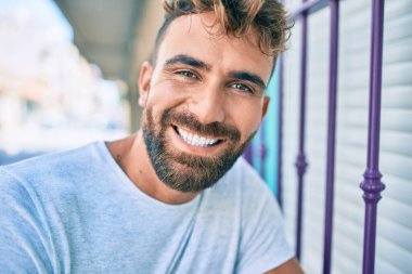 Genç İspanyol adam gülümsüyor. Mutlu bir şekilde şehrin duvarına yaslanıyor.