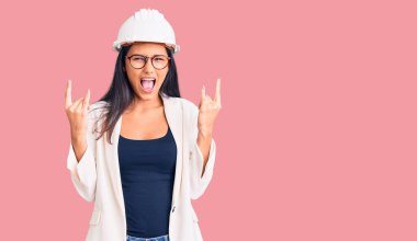 Mimar şapkalı, gözlüklü, çılgın bir ifadeyle bağıran genç, güzel bir Latin kız elleri havada rock sembolü yapıyor. Müzik yıldızı. ağır kavram. 