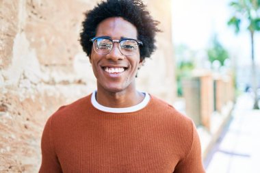 Genç, yakışıklı, Afro-Amerikalı, günlük kıyafetler ve mutlu gülümseyen gözlükler takıyor. Yüzünde tebessümle dikilip kameraya bakıyor ve caddede yürüyor..