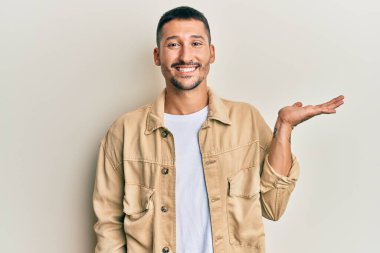 Dövmeleri olan, günlük kahverengi kot ceket giyen, neşeli gülümseyen, eli avucunda kameraya bakan yakışıklı bir adam.. 