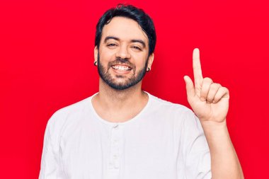 Bir fikir veya soruyla gülümseyen gündelik kıyafetler giyen genç İspanyol adam, bir numara, mutlu bir yüzle işaret ediyor. 