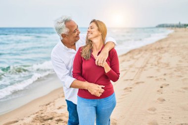 Orta yaşlı İspanyol çift mutlu bir şekilde gülüyor ve kumsalda yürüyorlar.