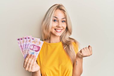 Güzel, beyaz, sarışın kız 50 Meksika pesosu tutuyor. Gururla bağırıyor, zaferi kutluyor ve başarıyı kollarını kaldırarak kutluyor. 