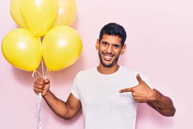Balonları tutan genç latin adam gülümseyen mutlu ve gururlu birini işaret ediyor. 