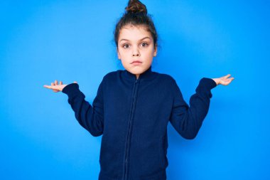 Sıradan kıyafetler giyen sevimli İspanyol çocuk, elleri ve kolları havada, kafası karışmış bir ifade. şüphe kavramı. 